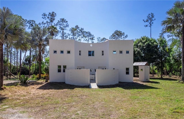 back of house with stucco siding, a lawn, and fence