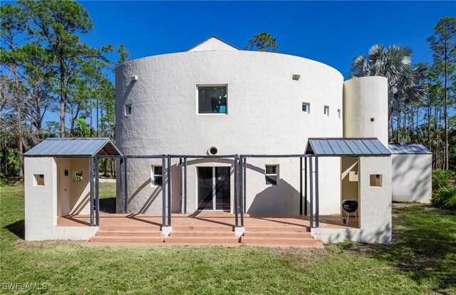 rear view of property featuring stucco siding, a yard, metal roof, and a standing seam roof