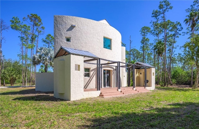 rear view of property featuring a standing seam roof, stucco siding, metal roof, and a yard