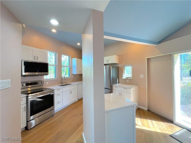 kitchen with light wood finished floors, appliances with stainless steel finishes, white cabinetry, and a sink