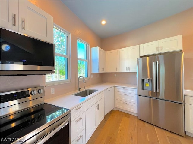 kitchen featuring a sink, white cabinetry, stainless steel appliances, light wood-style floors, and light countertops