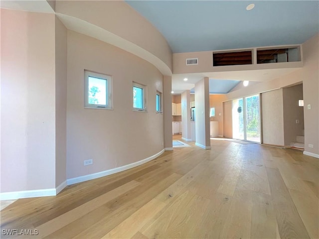 spare room featuring light wood finished floors, visible vents, baseboards, and vaulted ceiling