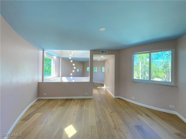 spare room with plenty of natural light, baseboards, visible vents, and wood finished floors