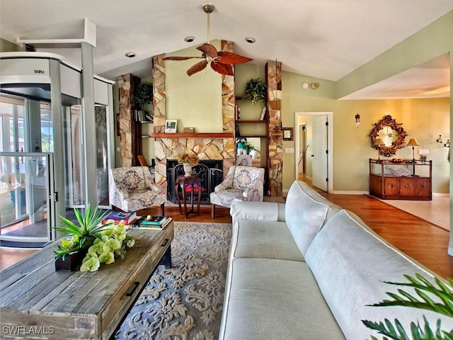 living area with lofted ceiling, a ceiling fan, wood finished floors, a stone fireplace, and baseboards