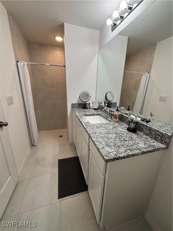 bathroom with vanity, tile patterned flooring, baseboards, and a tile shower