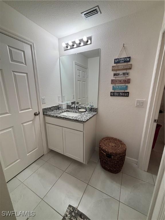 bathroom featuring tile patterned floors, visible vents, a textured ceiling, vanity, and a textured wall