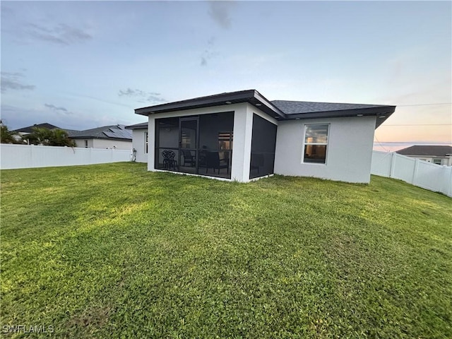 rear view of house with stucco siding, a yard, a fenced backyard, and a sunroom