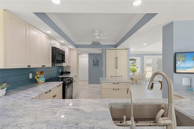 kitchen with light stone counters, ornamental molding, a sink, black appliances, and a raised ceiling