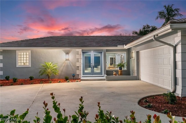 view of exterior entry with concrete driveway, an attached garage, french doors, and stucco siding