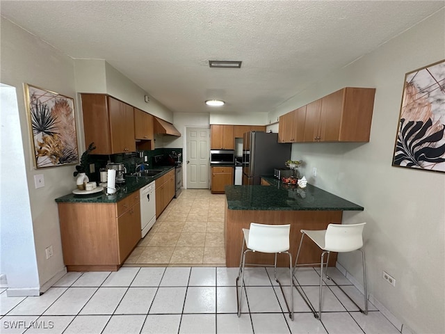 kitchen featuring a peninsula, a sink, stainless steel appliances, a textured ceiling, and dark countertops