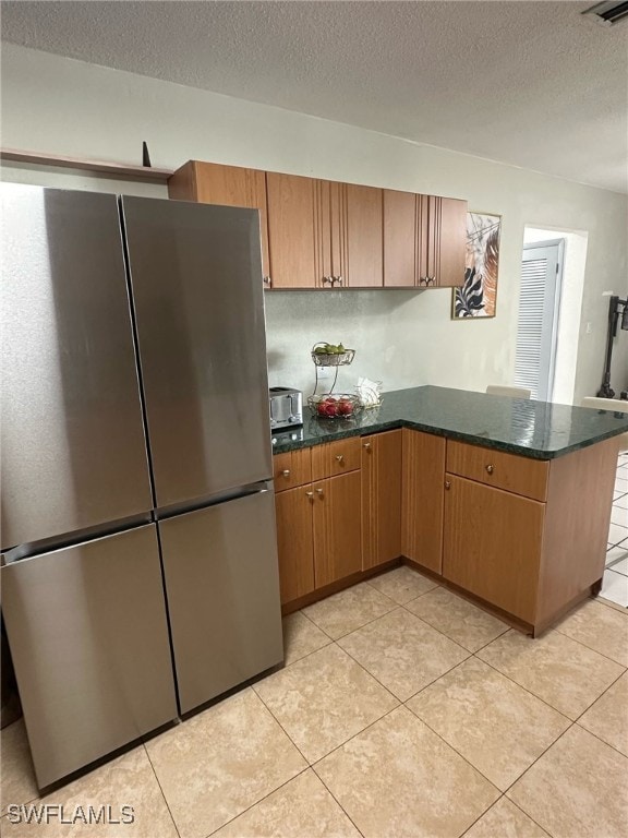 kitchen with a peninsula, light tile patterned floors, dark stone countertops, and freestanding refrigerator