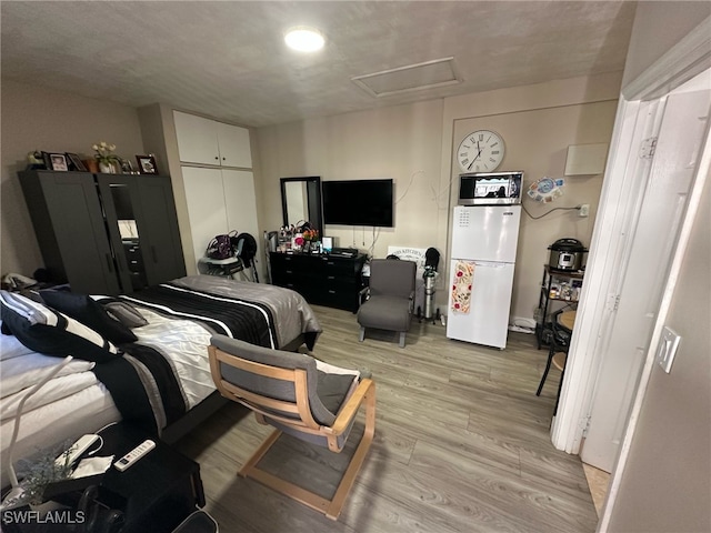 bedroom featuring attic access, light wood-style flooring, and freestanding refrigerator