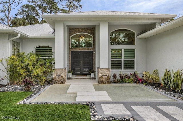 view of exterior entry featuring a standing seam roof, stucco siding, french doors, stone siding, and metal roof