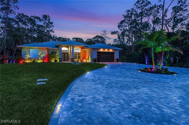 view of front of house with stucco siding, decorative driveway, a garage, and a yard