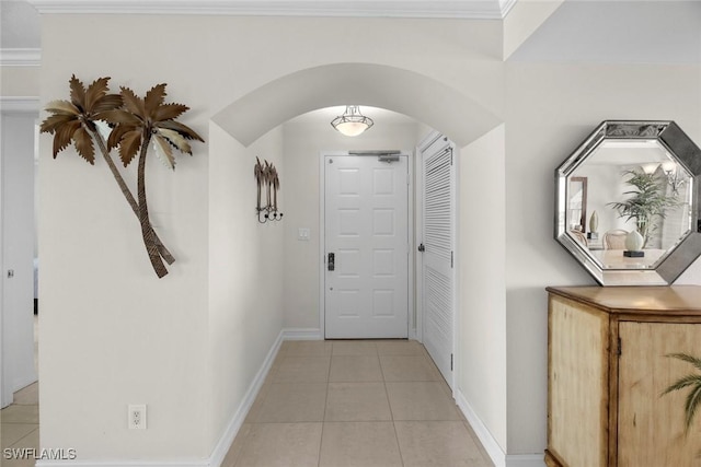 hall featuring light tile patterned floors, baseboards, arched walkways, and crown molding