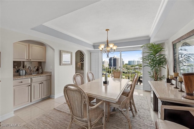 dining room with baseboards, a tray ceiling, arched walkways, a notable chandelier, and a view of city