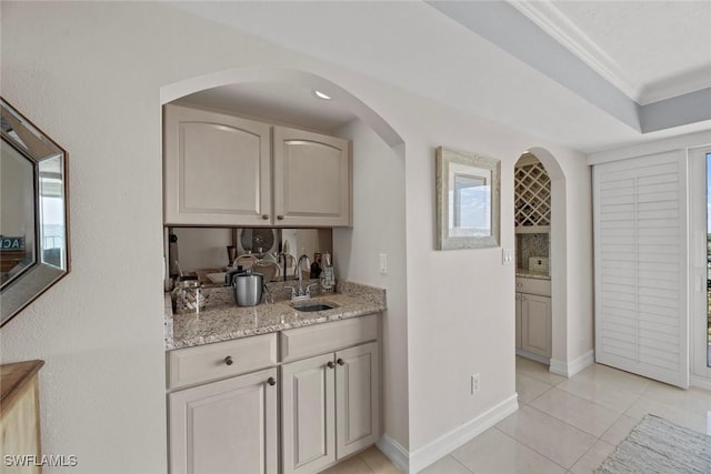 interior space featuring ornamental molding, a sink, arched walkways, light tile patterned floors, and baseboards