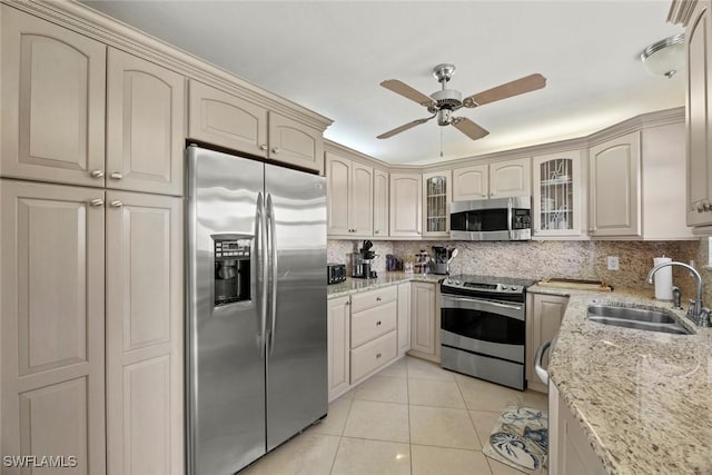 kitchen featuring light tile patterned floors, a ceiling fan, a sink, appliances with stainless steel finishes, and backsplash