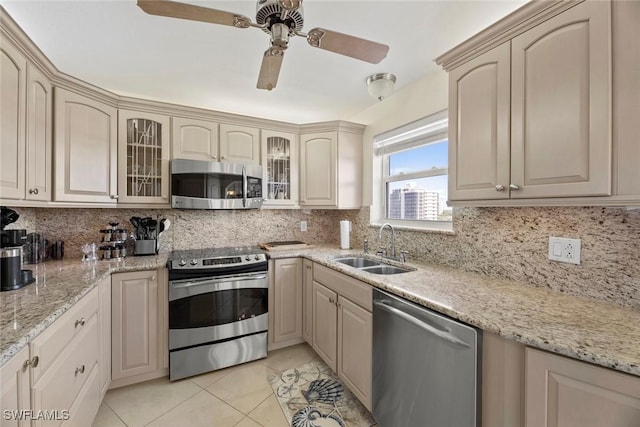 kitchen with a sink, glass insert cabinets, appliances with stainless steel finishes, light tile patterned flooring, and decorative backsplash