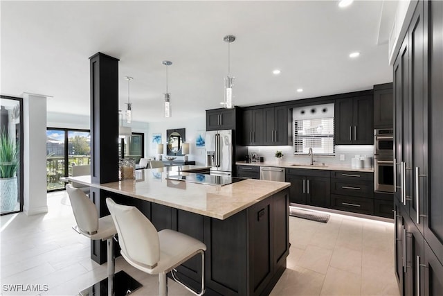 kitchen featuring light stone countertops, a sink, appliances with stainless steel finishes, decorative light fixtures, and backsplash