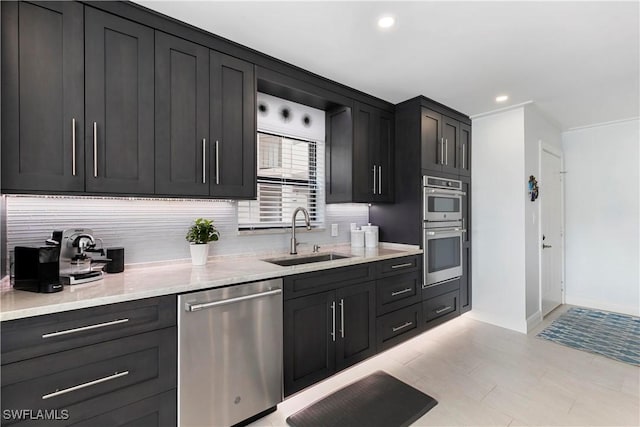 kitchen with a sink, backsplash, appliances with stainless steel finishes, light stone countertops, and dark cabinets