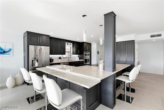 kitchen featuring a breakfast bar area, visible vents, a sink, stainless steel appliances, and decorative light fixtures