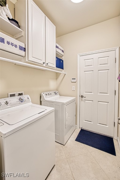 laundry area featuring light tile patterned floors, cabinet space, and washer and clothes dryer