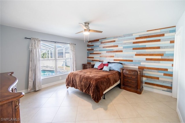 tiled bedroom featuring ceiling fan, an accent wall, and baseboards