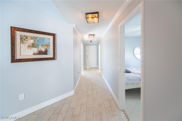 hallway featuring light wood finished floors, crown molding, and baseboards