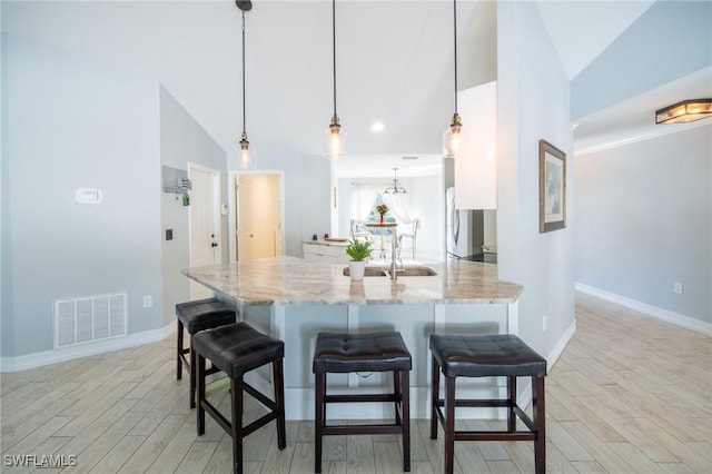 kitchen with light stone countertops, visible vents, white cabinetry, a kitchen breakfast bar, and light wood-type flooring