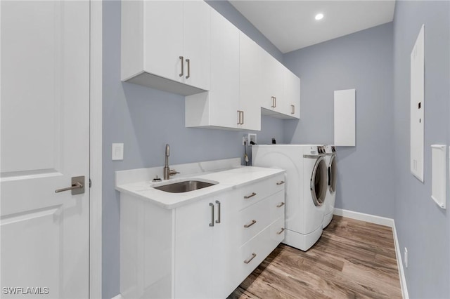 clothes washing area with a sink, wood finished floors, cabinet space, separate washer and dryer, and baseboards