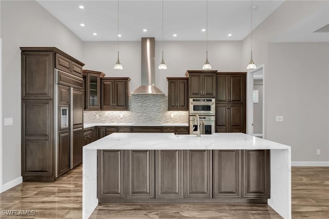 kitchen with paneled fridge, stainless steel double oven, dark brown cabinetry, wall chimney exhaust hood, and tasteful backsplash