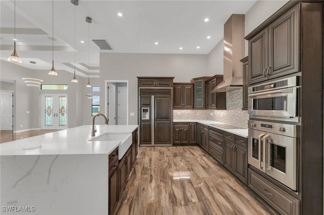 kitchen featuring backsplash, electric stovetop, wall chimney exhaust hood, paneled refrigerator, and a sink