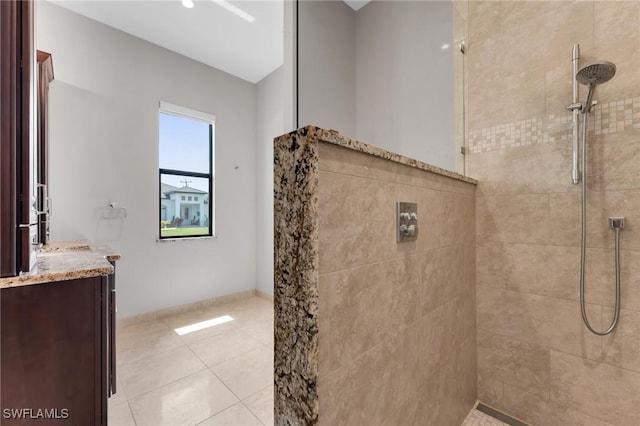 bathroom with baseboards, tiled shower, vanity, and tile patterned flooring