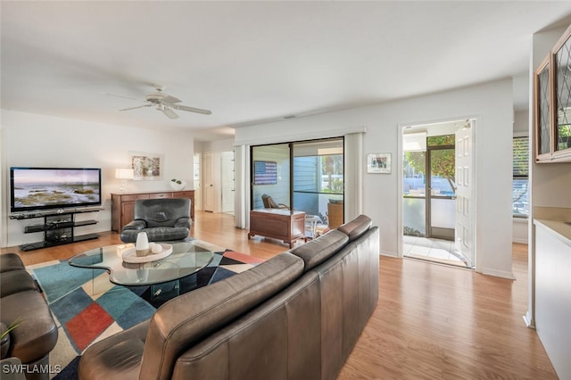 living area featuring baseboards, light wood finished floors, and ceiling fan