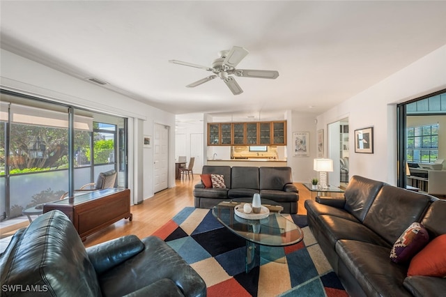 living room with visible vents, light wood finished floors, and ceiling fan