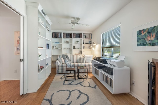 living area with baseboards, ceiling fan, and wood finished floors