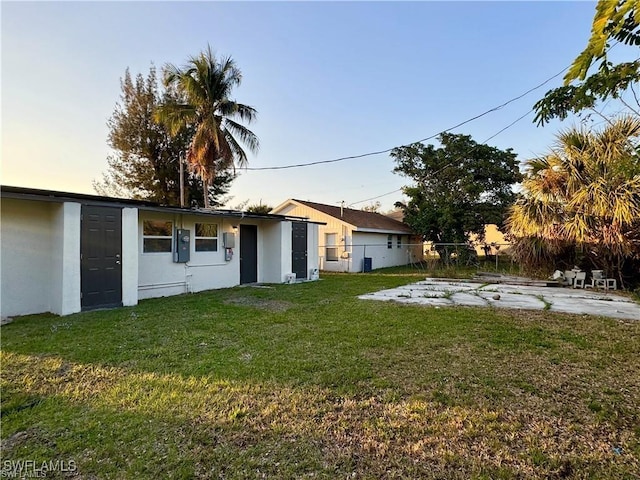 rear view of house featuring a yard, fence, and stucco siding