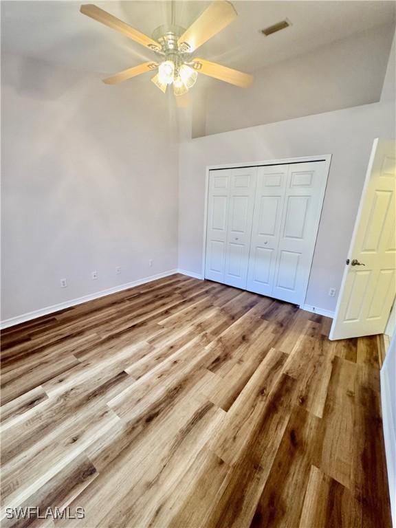 unfurnished bedroom featuring a ceiling fan, visible vents, wood finished floors, baseboards, and a closet