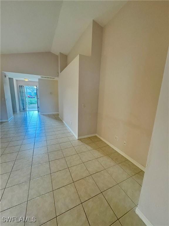 empty room featuring light tile patterned floors, baseboards, and vaulted ceiling