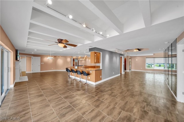 unfurnished living room with rail lighting, beamed ceiling, baseboards, and a ceiling fan