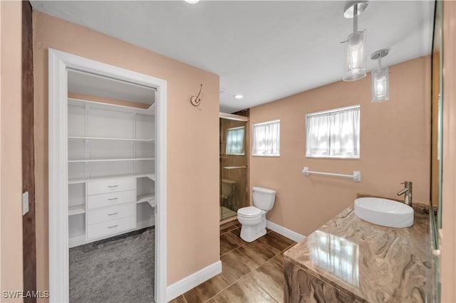 full bath with a shower stall, a walk in closet, baseboards, toilet, and vanity