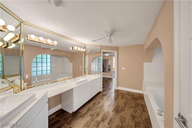 full bathroom with baseboards, vanity, ceiling fan, and a tub to relax in