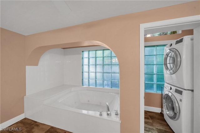 bathroom with tile patterned floors, stacked washer / dryer, baseboards, and a whirlpool tub