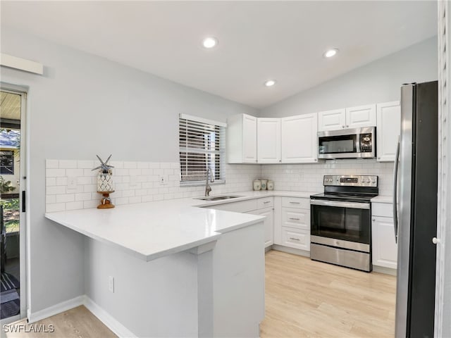 kitchen featuring a sink, white cabinetry, stainless steel appliances, a peninsula, and vaulted ceiling