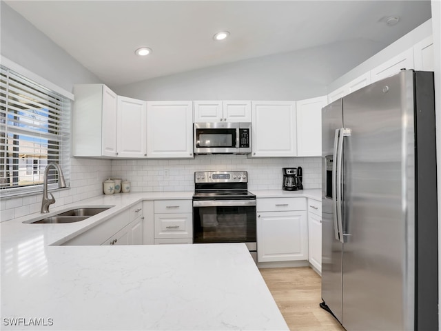 kitchen with lofted ceiling, a sink, decorative backsplash, stainless steel appliances, and white cabinets