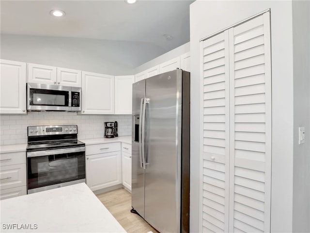 kitchen with stainless steel appliances, lofted ceiling, tasteful backsplash, and white cabinets