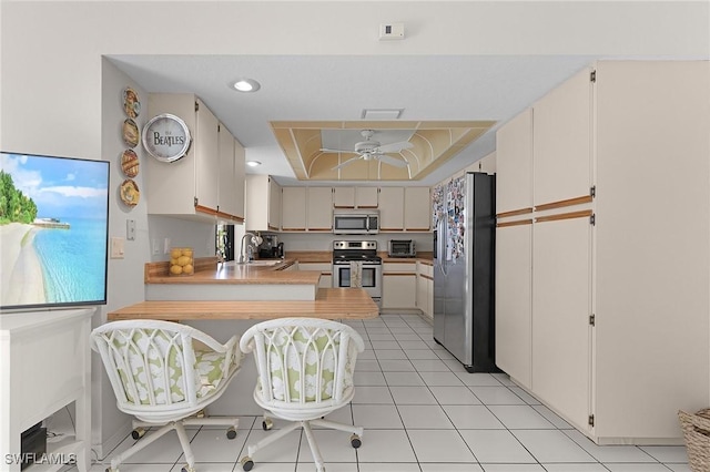 kitchen with light countertops, appliances with stainless steel finishes, a peninsula, a ceiling fan, and a sink