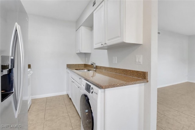 kitchen featuring stainless steel fridge with ice dispenser, dark stone countertops, washer / dryer, white cabinets, and a sink