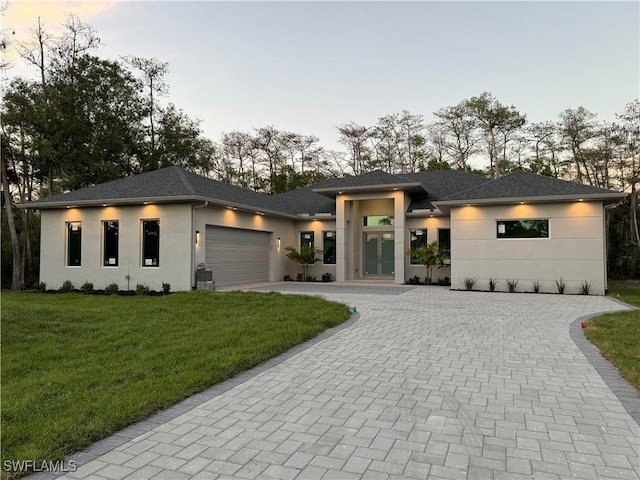 prairie-style home with decorative driveway, a garage, a front lawn, and stucco siding